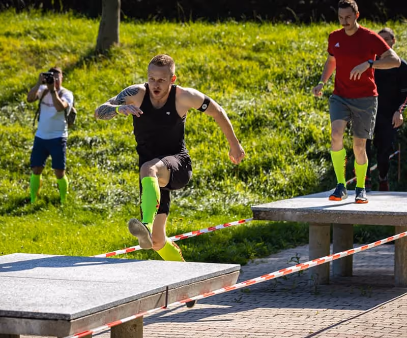 Erz-X-Cross Teilnehmer springen auf Beton-Tischtennisplatten, welche als Hindernis dienen.