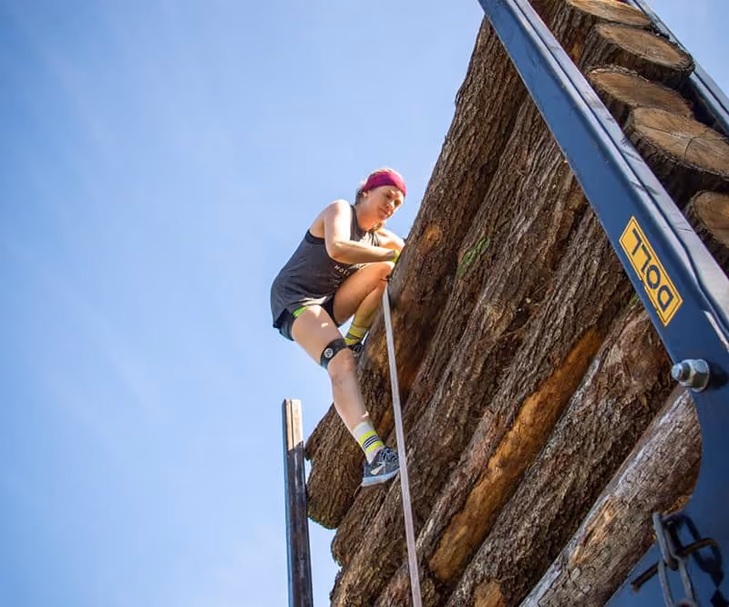 Eine Erz-X-Cross Teilnehmerin klettert über einen Lkw, welcher mit Holzstämmen beladen wurde.