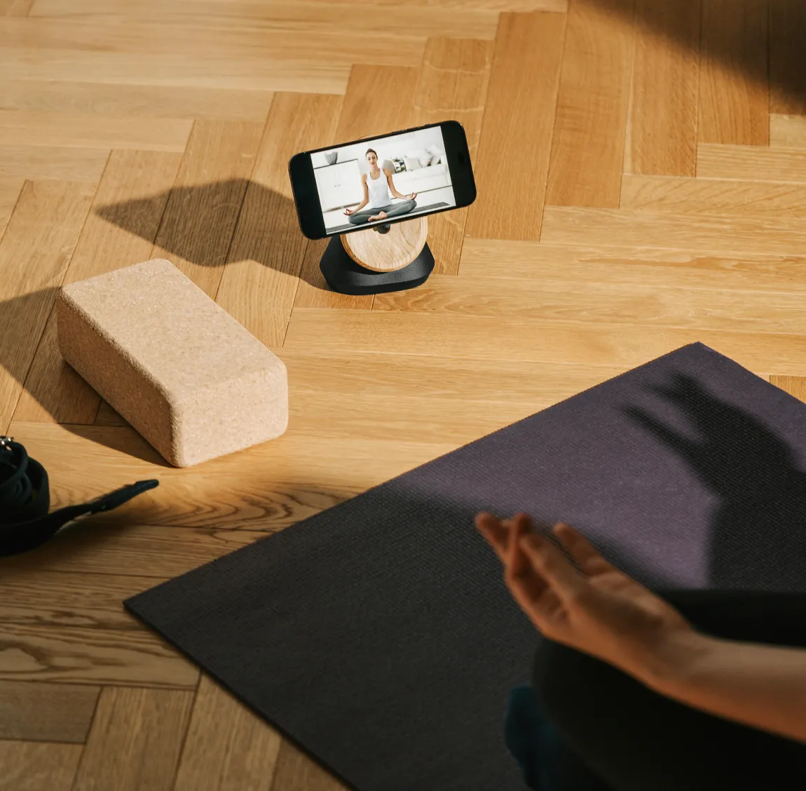Smartphone displaying a virtual fitness session on a wooden floor next to a yoga mat and block, representing mobile health apps, digital fitness solutions, and scalable healthcare technology.