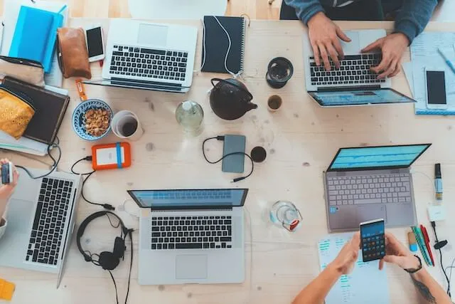 Ein Tisch mit mehreren Laptops an denen im Team gearbeitet wird