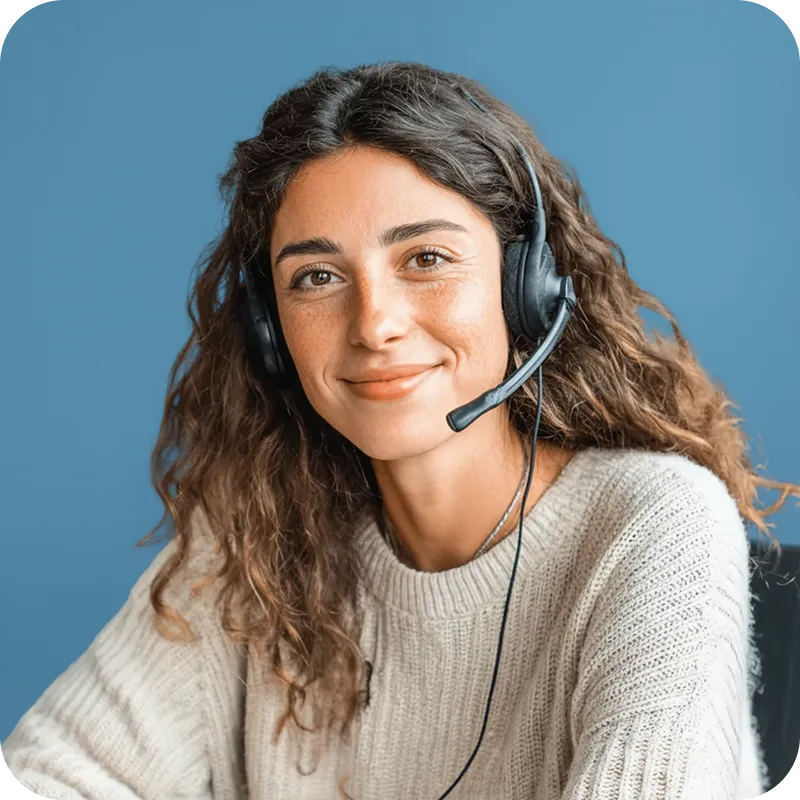 Eine lächelnde Frau mit einem professionellen Headset und einem Strickpullover vor einer blauen Wand.