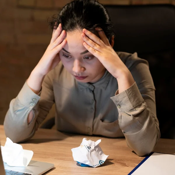 Une femme assise à un bureau, la tête dans les mains, exprimant de la frustration ou du stress.