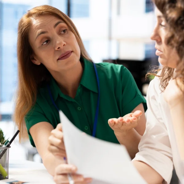 Deux femmes discutent dans un bureau, échangeant des idées dans un environnement professionnel.