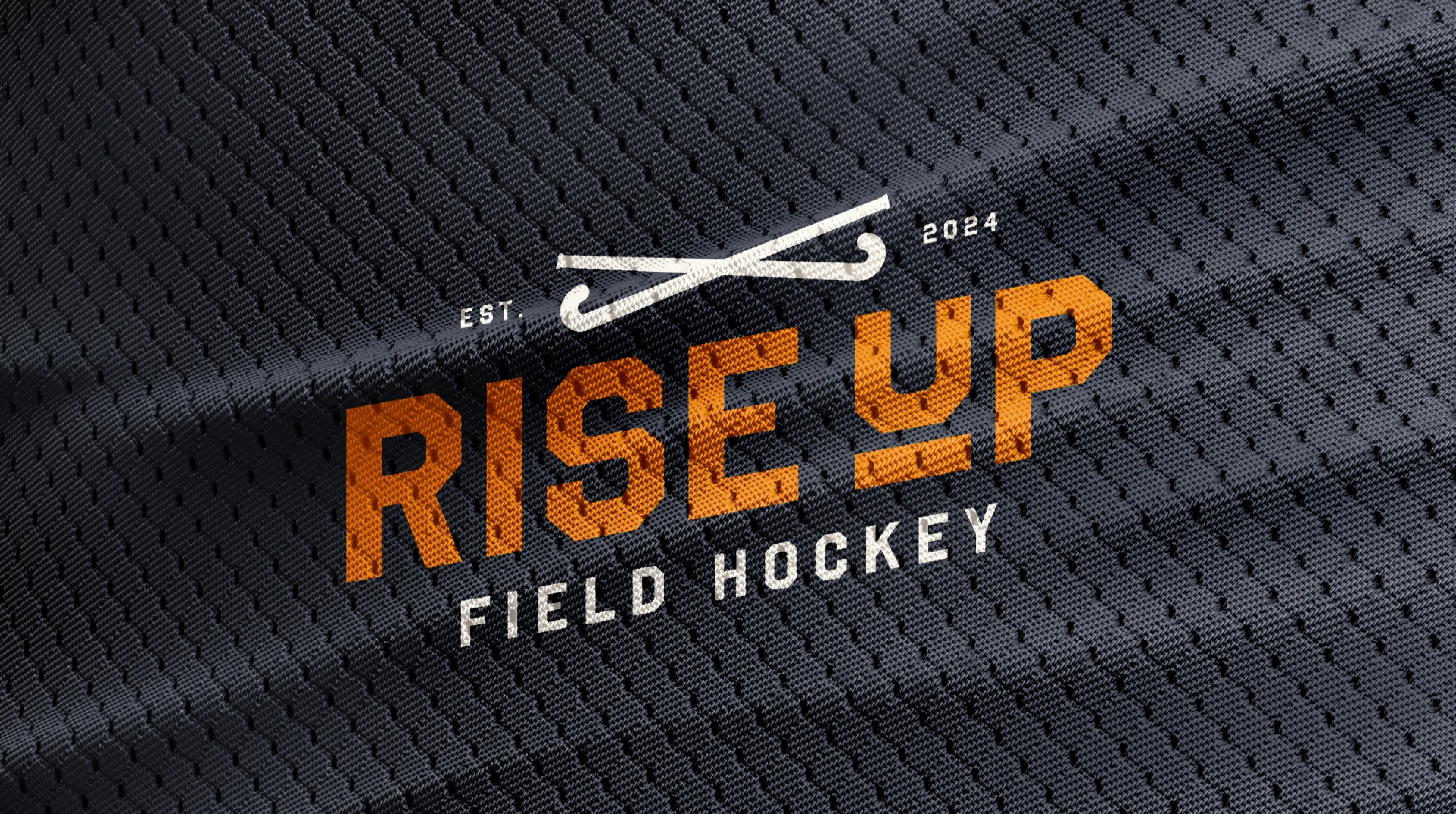 Dark textured fabric with orange text saying 'RISE UP' and white text below saying 'FIELD HOCKEY' with two crossed hockey sticks above.