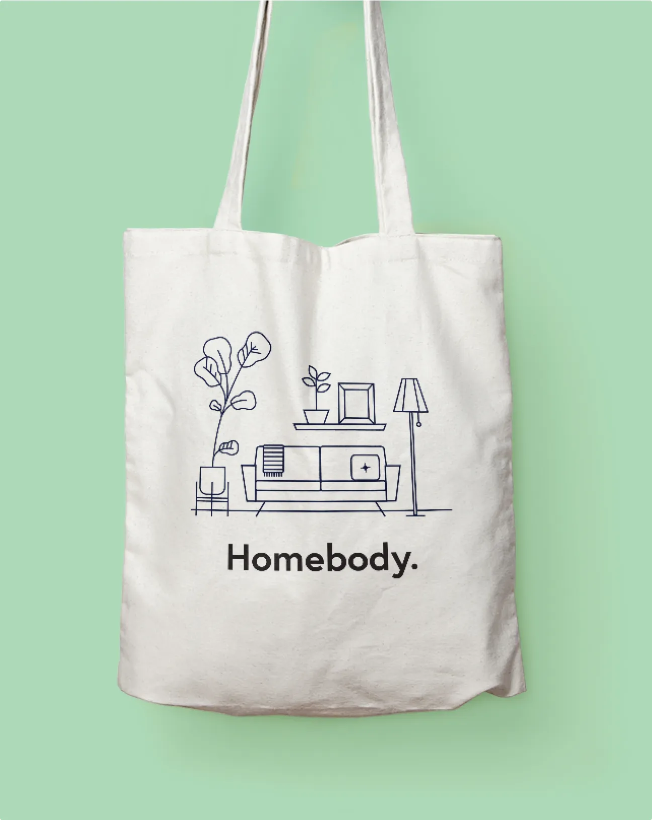 White tote bag with a minimalist line drawing of a living room featuring a sofa, plants, a shelf, and a floor lamp, with the word 'Homebody.' below.