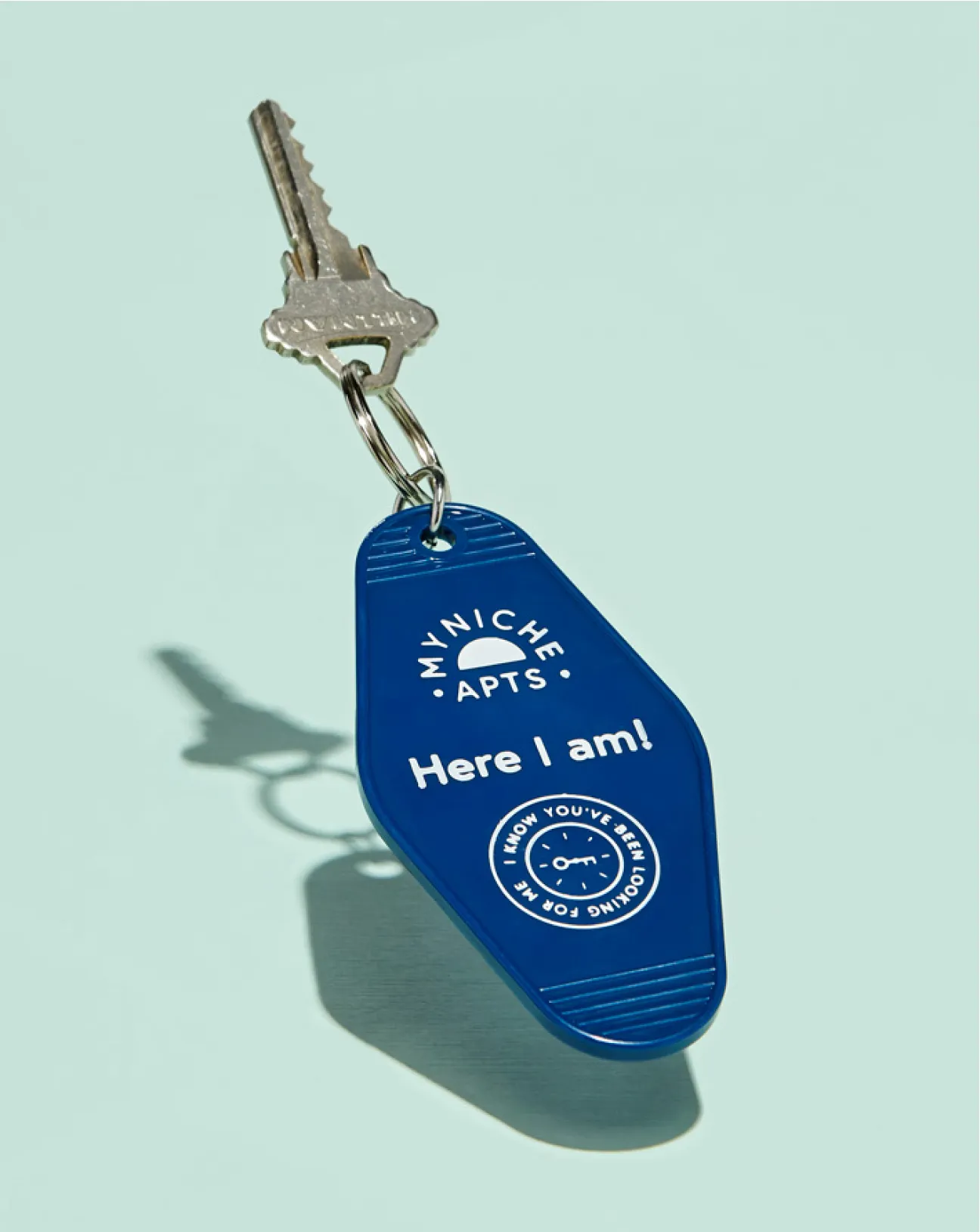 Silver key attached to a blue keychain that says 'MYNICHE APTS. Here I am!' with a clock and key logo.