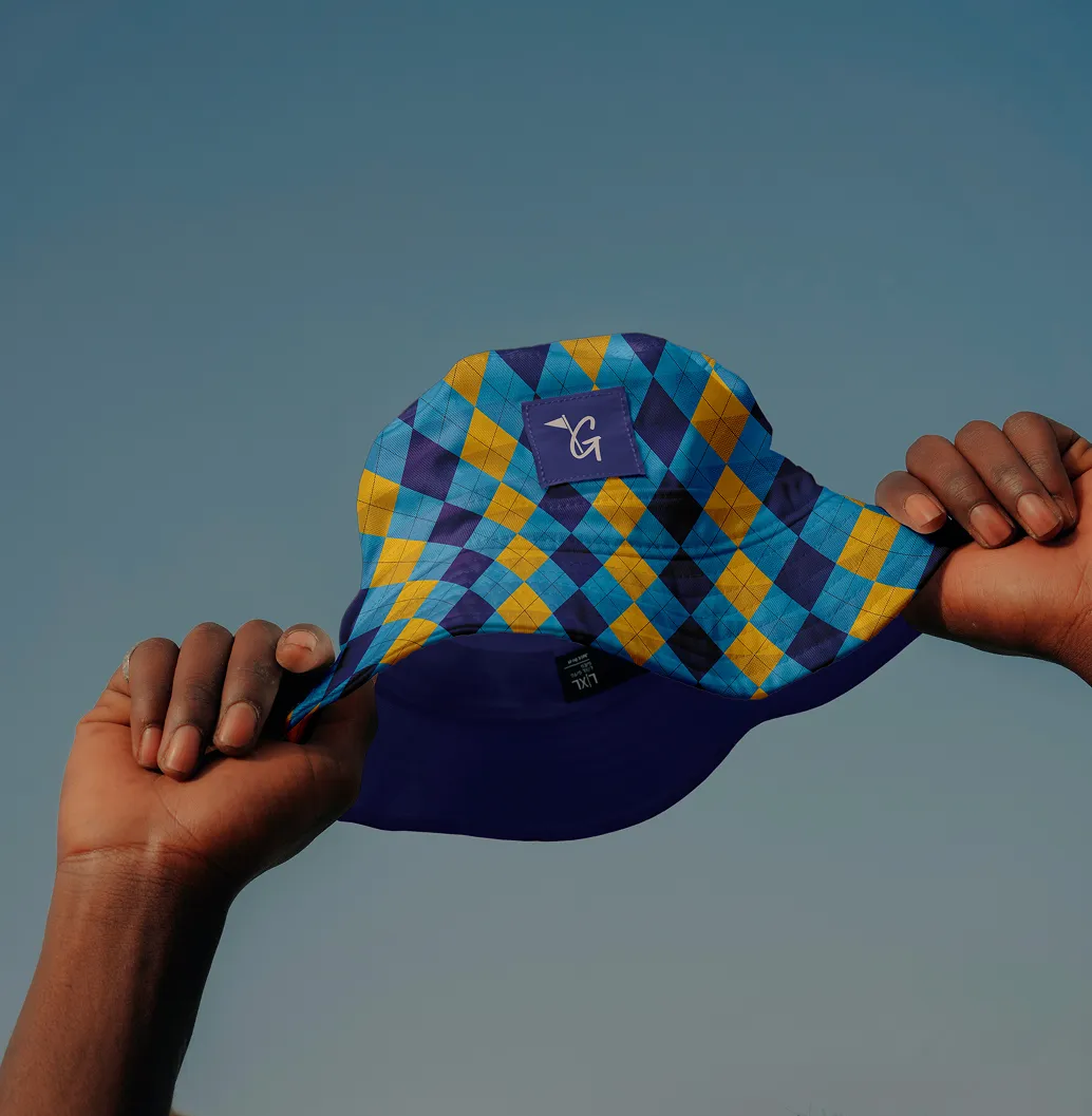 Person holding a blue, yellow, and purple argyle-patterned bucket hat against a clear sky.