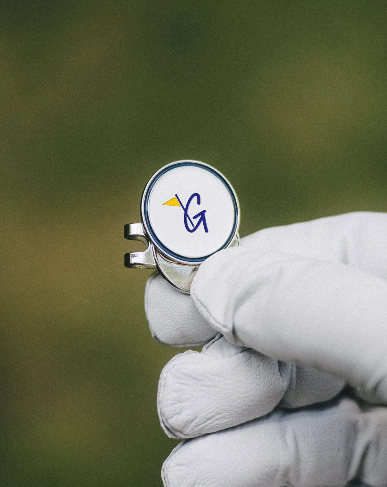 Gloved hand holding a silver object with a white circular face displaying a stylized blue letter G and a small yellow triangle.