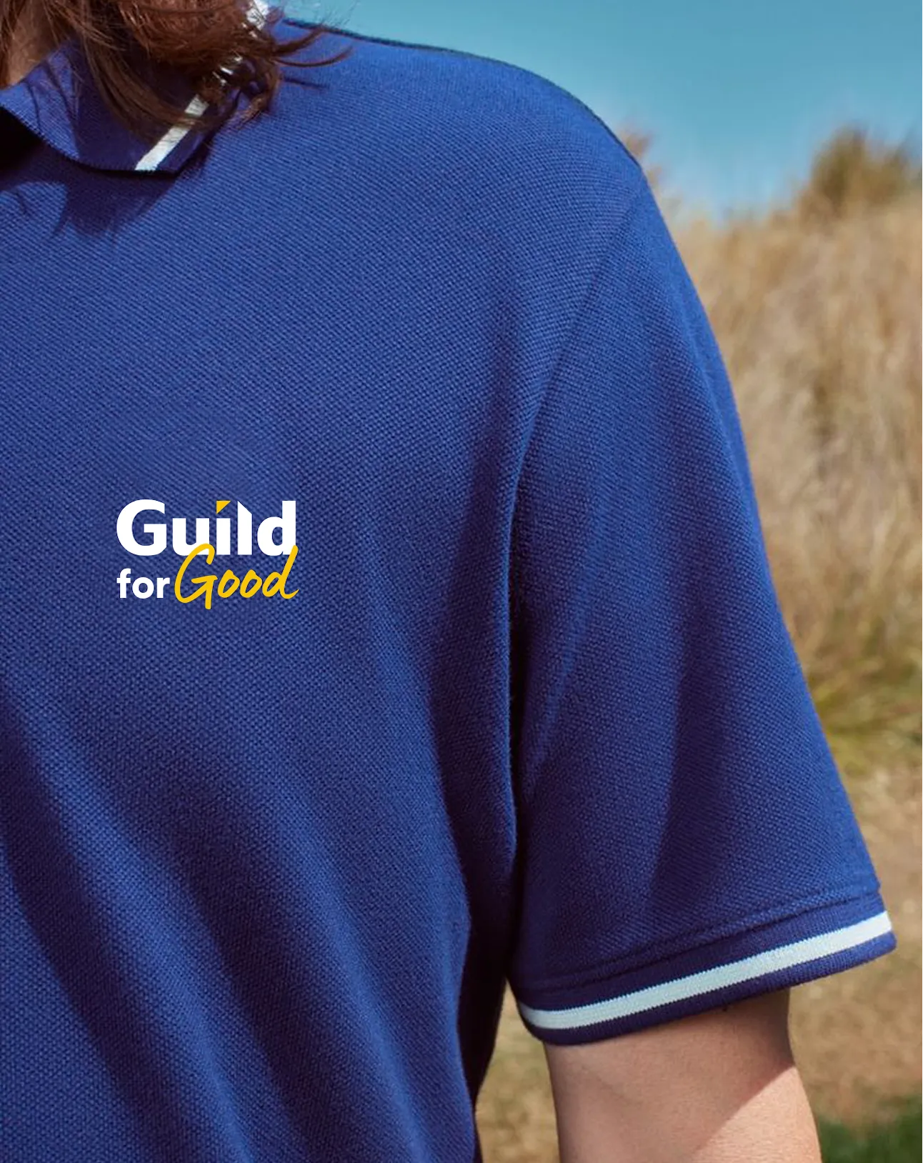 Close-up of a person wearing a blue polo shirt with white and light blue striped sleeve cuffs and a 'Guild for Good' logo on the chest.