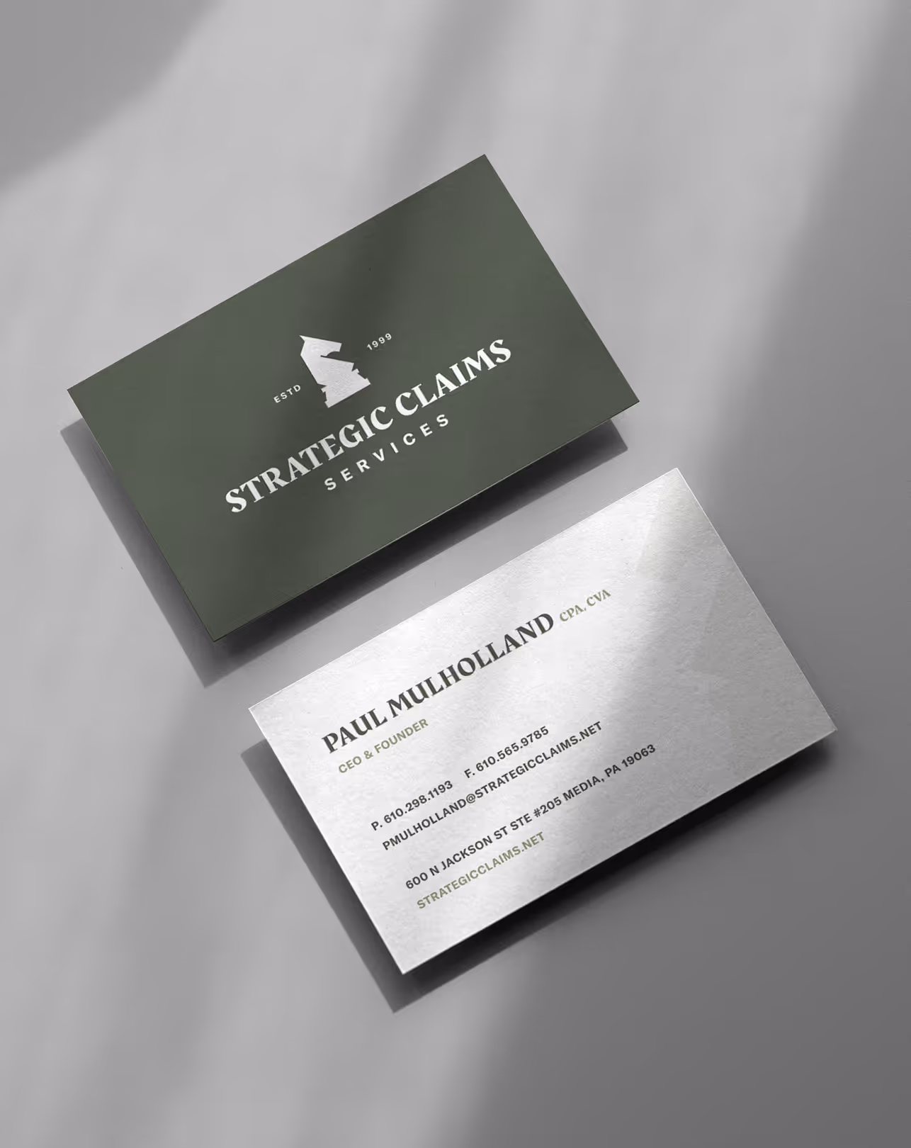 Two business cards for Strategic Claims Services; one dark with the company logo and name, and one white with contact details for Paul Mulholland, CEO and Founder.