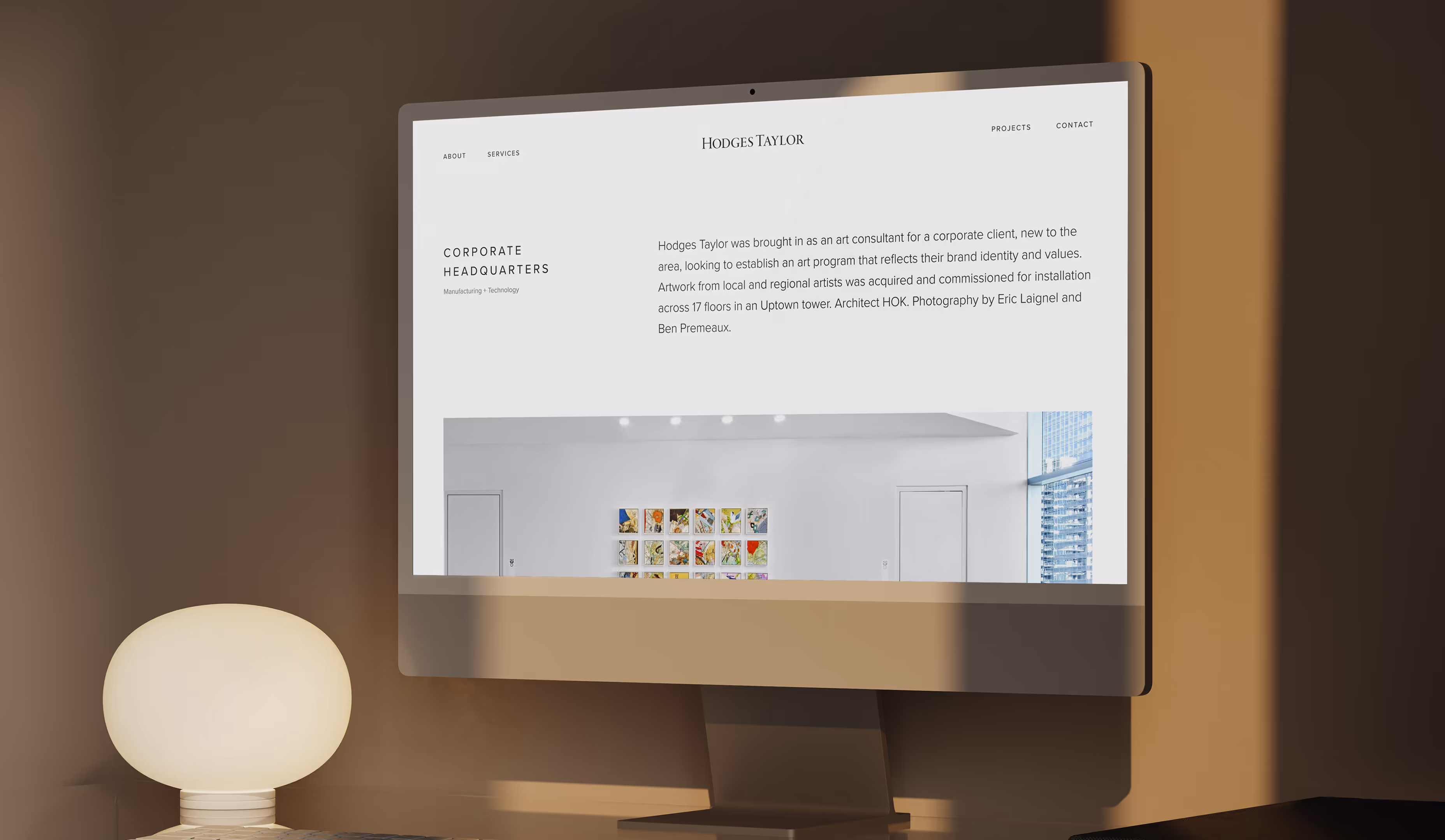 Desktop computer on desk displaying Hodges Taylor website featuring corporate headquarters art consultancy and project description.