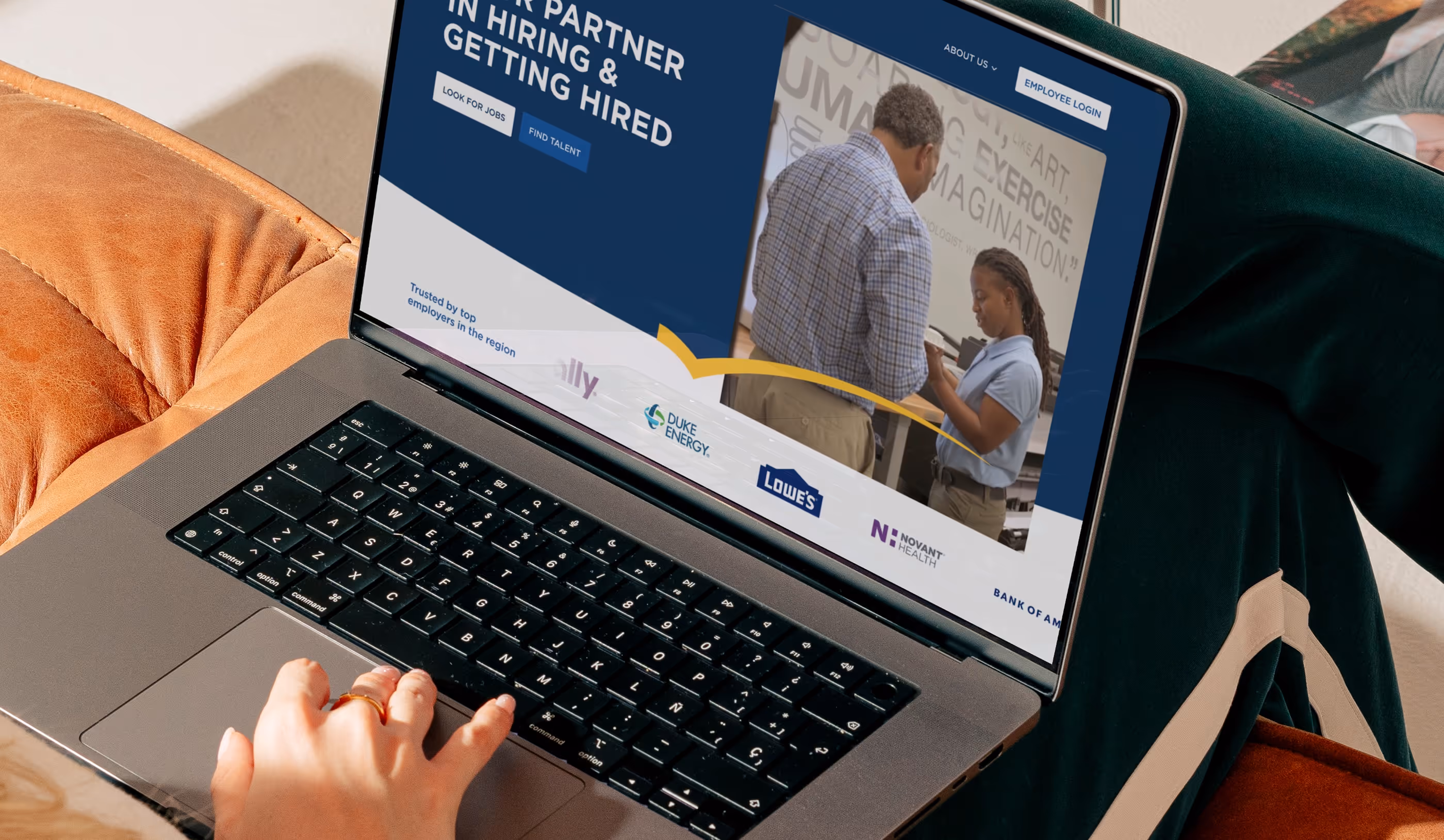 Person using a laptop displaying a hiring and job search website featuring corporate logos and a photo of two people discussing work.