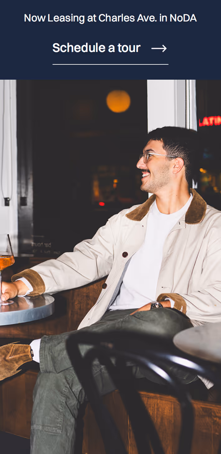 Man in glasses sitting at a table with a drink, smiling and looking to the side in a cozy indoor setting.