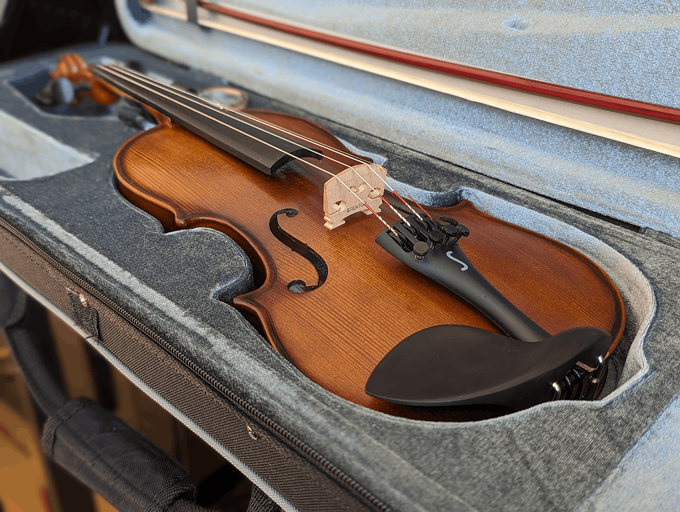 Brown violin with black chin rest and fine tuners resting inside a gray padded hard case with its bow secured in the lid.