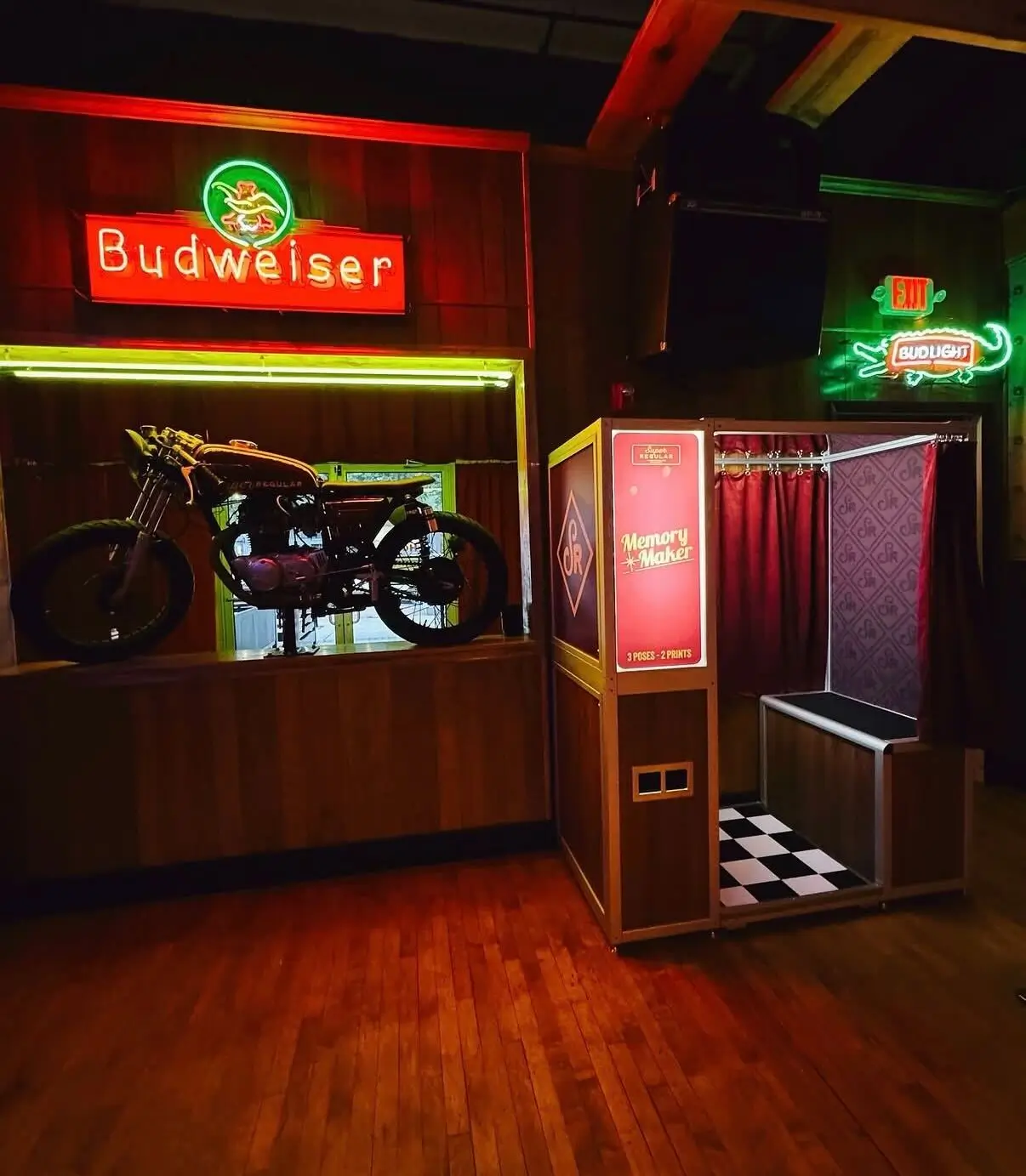 Vintage photo booth in bar by Majestic Photobooth. Dark wood grain and red velvet curtain photo booth in a bar with a Budweiser sign above it.