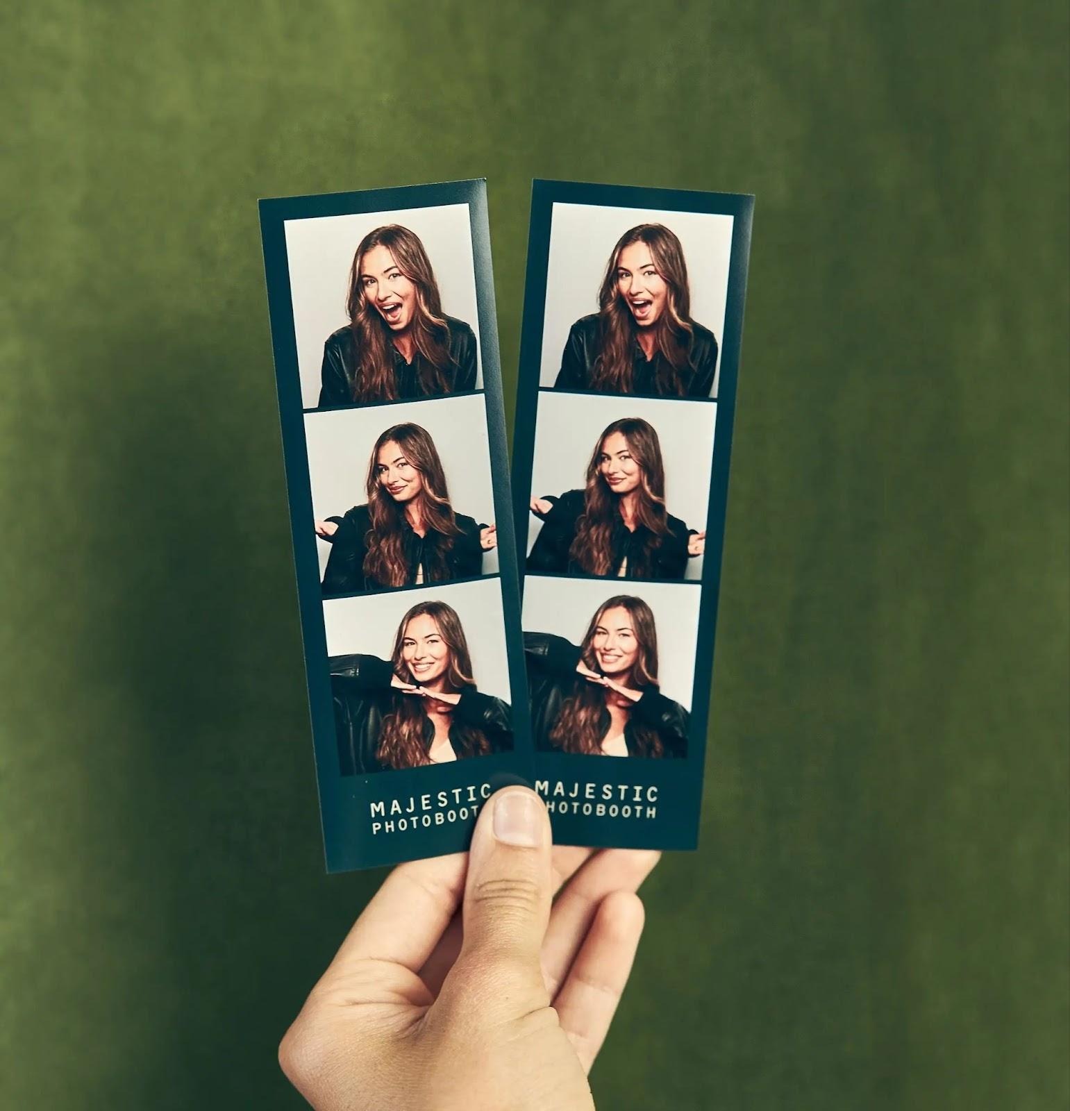 Photo-of a hand holding two Majestic Photobooth strips on a green background.