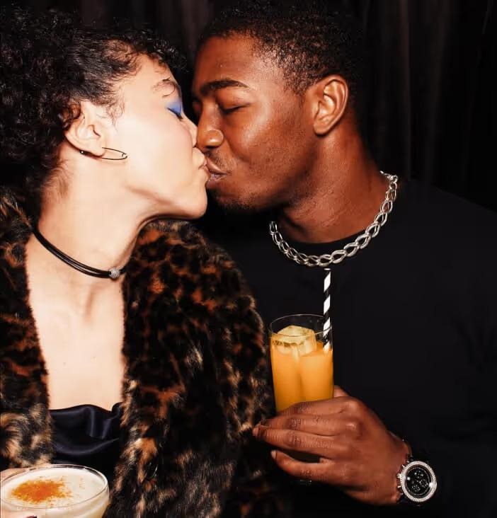 Photo-close up of a couple kissing at a nightclub holding cocktails.
