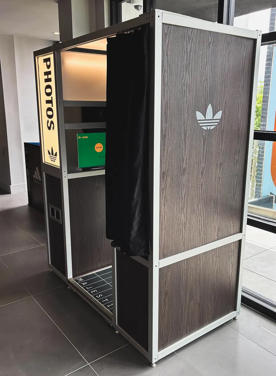 Angled view of the wood grain Adidas photo booth showing black curtain entrance and branded sign