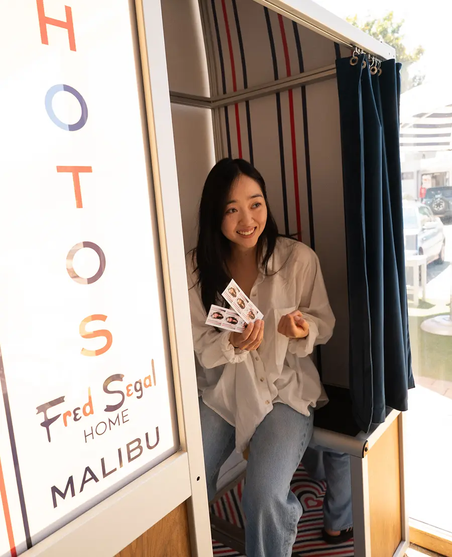 Guest laughing inside the Fred Segal Home Malibu photo booth holding printed photo strips
