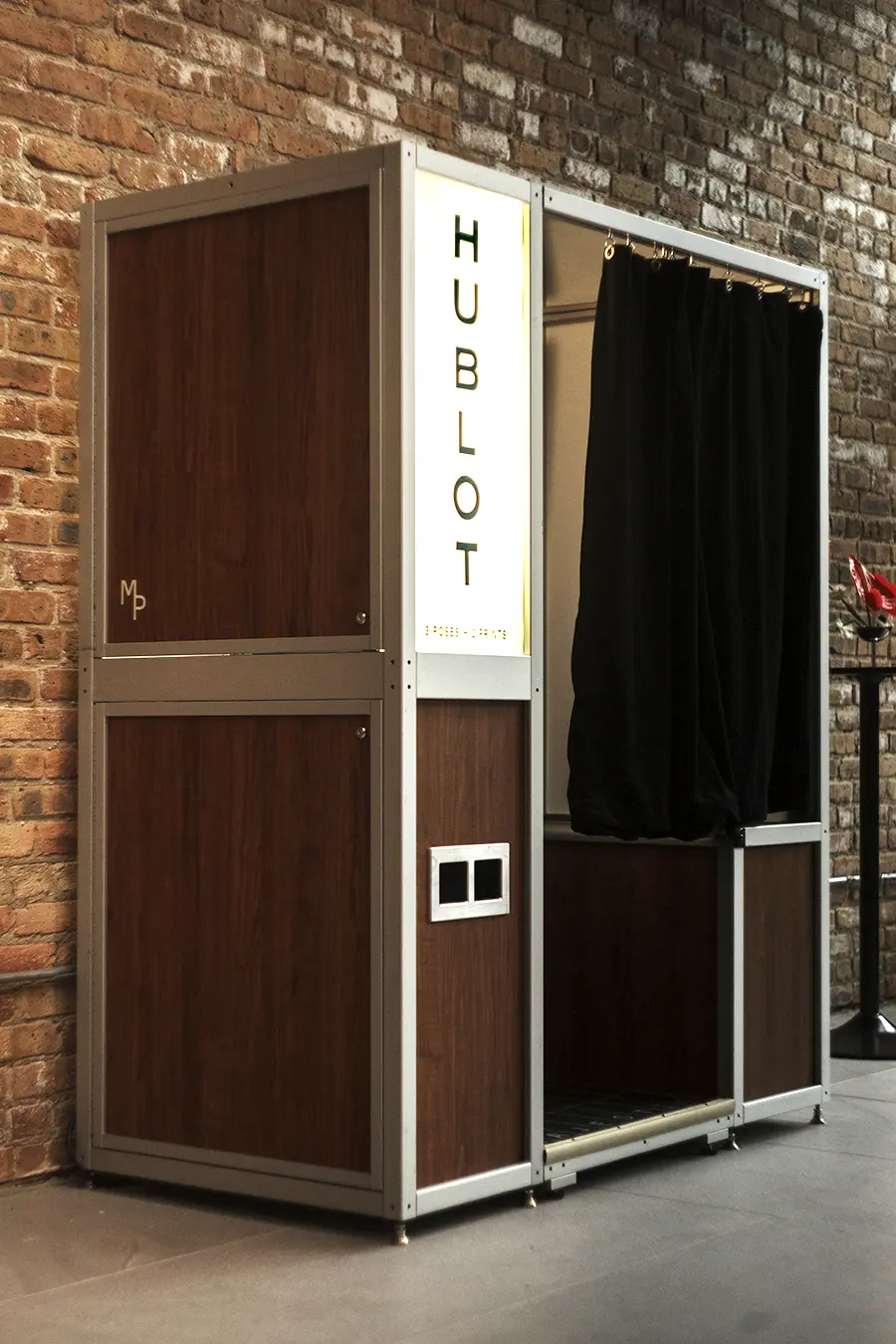 Custom walnut photo booth with an illuminated Hublot marquee installed against original Chicago brick at the Fulton Market boutique opening