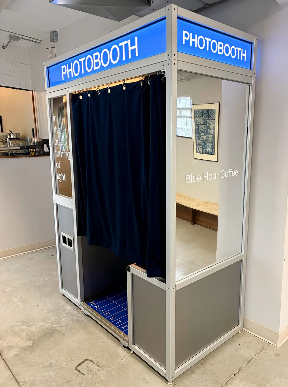 Mirrored side panel of the Blue Hour Coffee photo booth reflecting the cafe interior, with navy velvet curtain and blue Majestic floor plate