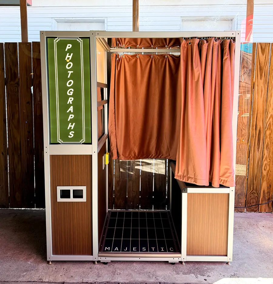 Photo booth with an olive green PHOTOGRAPHS panel and terracotta velvet curtain installed on the patio at Radio Rosewood in Austin