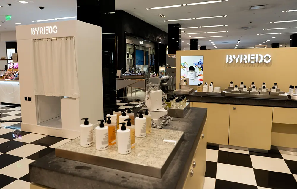 Custom built white Byredo photo booth beside the Byredo fragrance counter on the beauty floor at Bloomingdale's, on a checkerboard floor