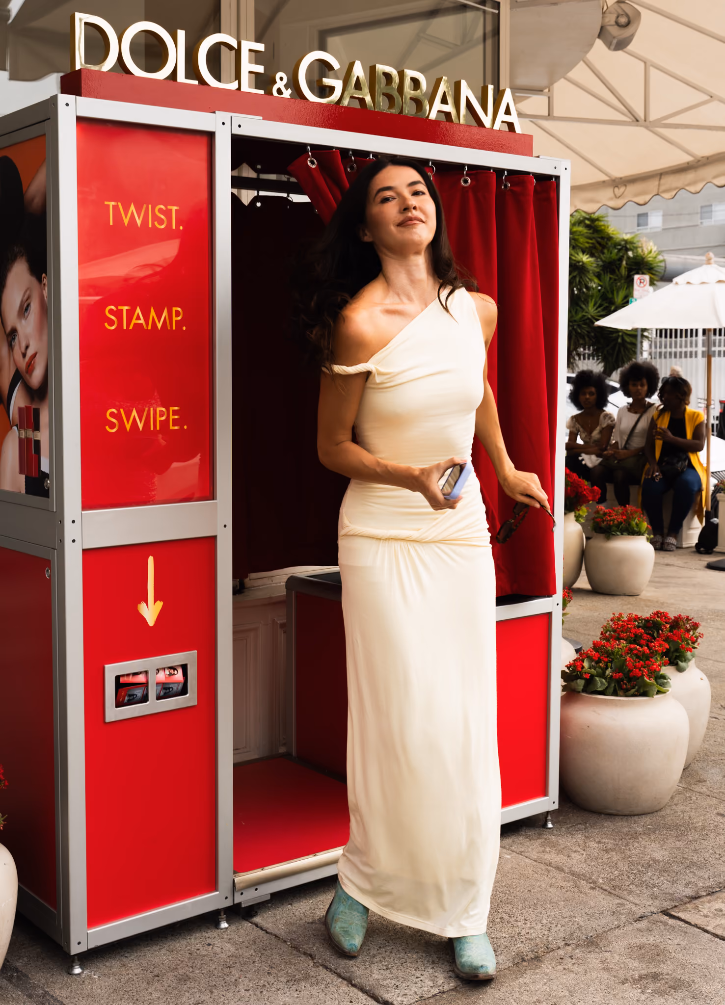 A guest stepping out of the red Dolce & Gabbana Beauty photo booth on the sidewalk in Los Angeles, with the red velvet curtain behind her