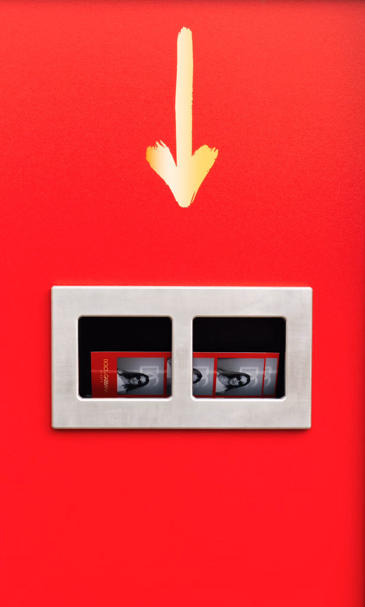 Gold hand painted arrow above the brushed steel print slot on the red Dolce & Gabbana photo booth, with two red photo strips in the tray
