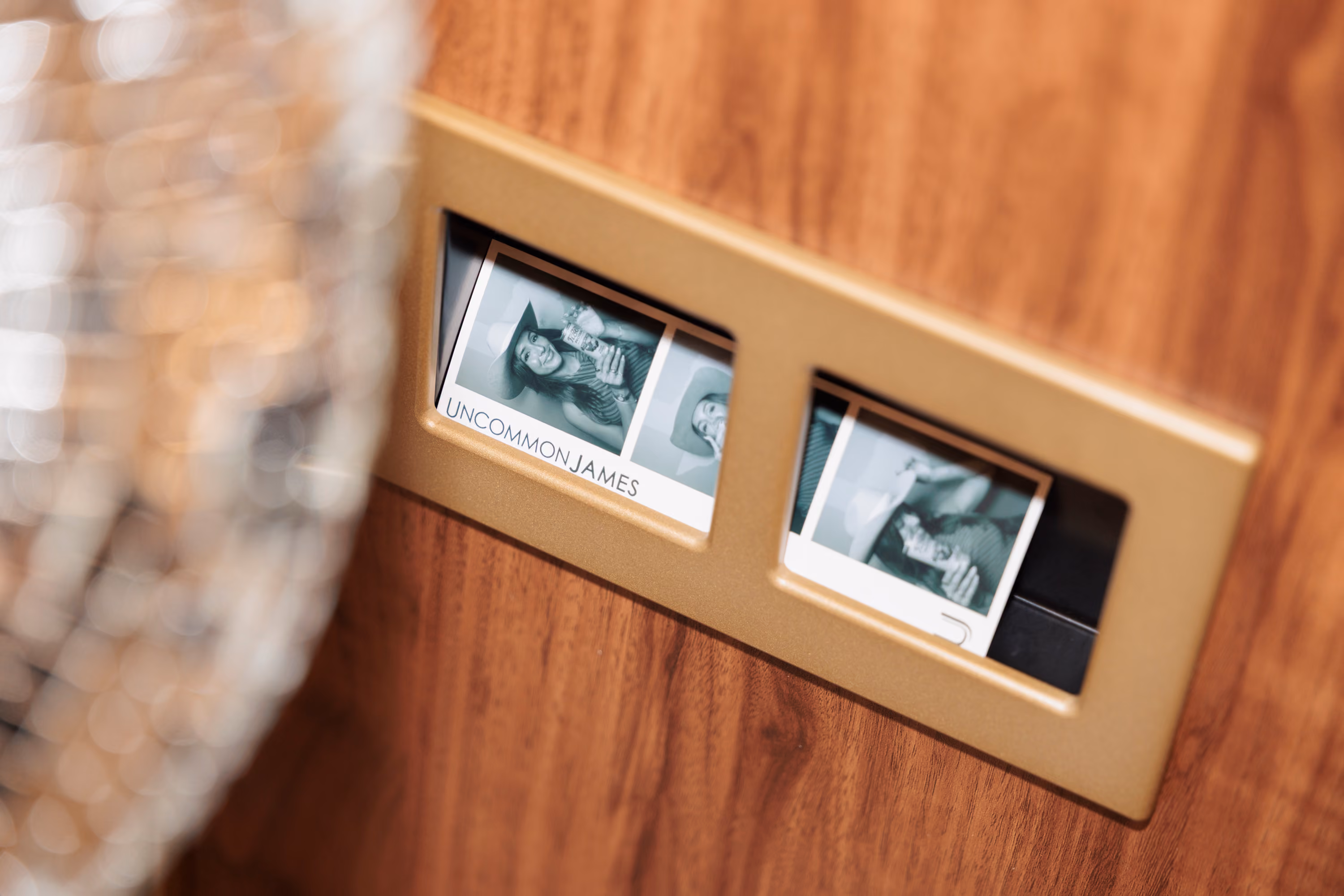 Two Uncommon James photo strips in the brass print tray of the photo booth, set into a walnut panel