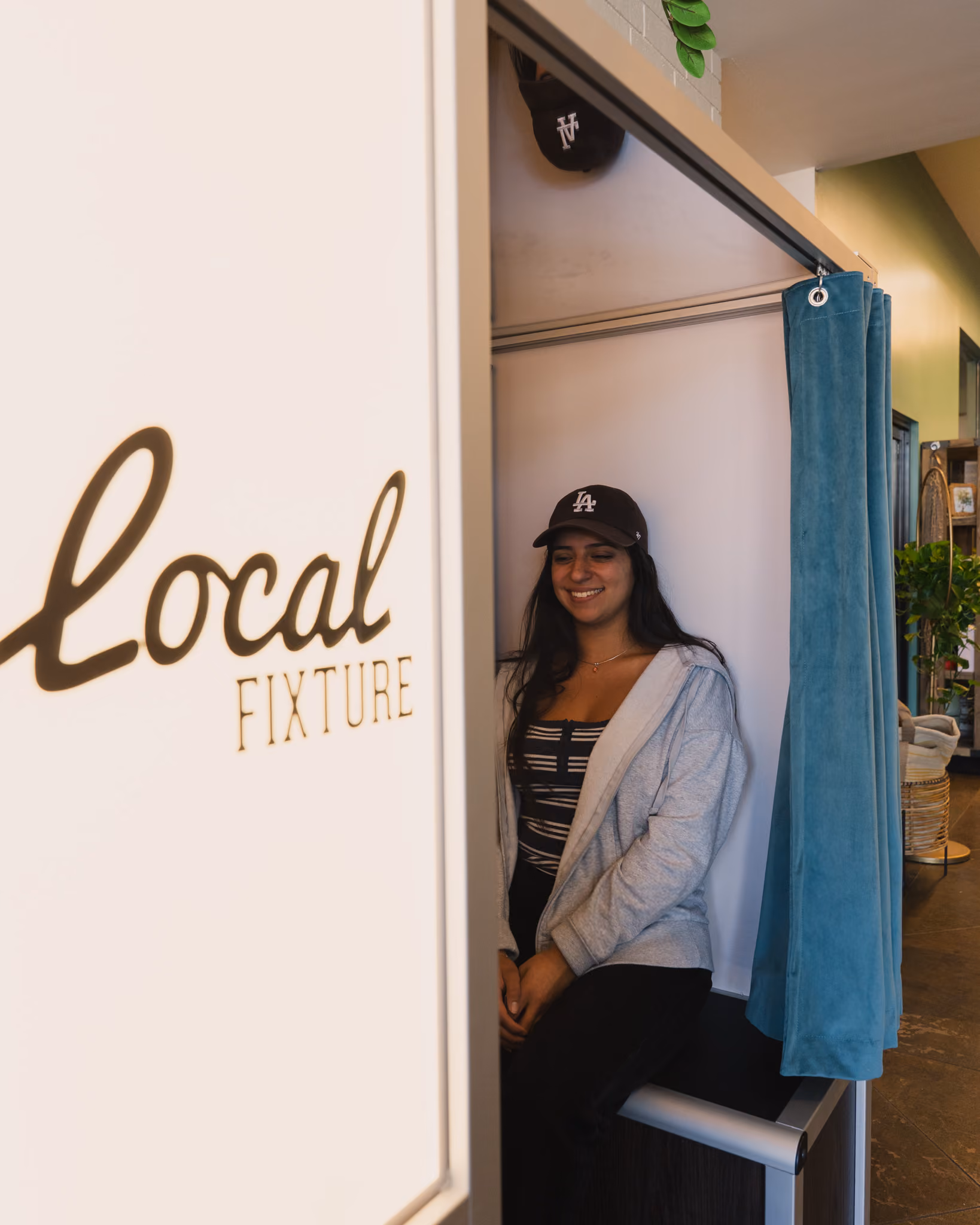 A guest sitting inside the Local Fixture photo booth behind the teal velvet curtain