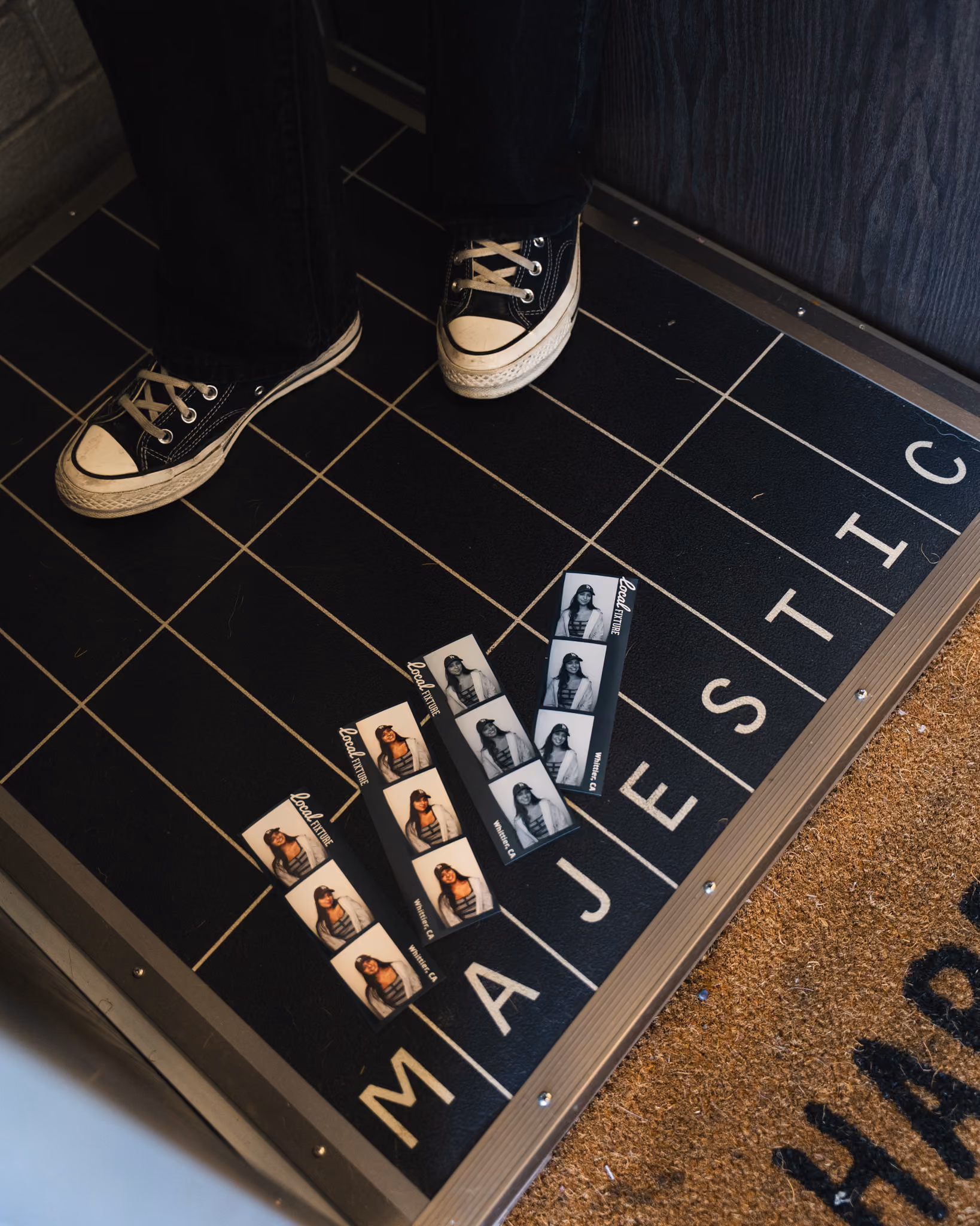 Four Local Fixture photo strips on the black grid floor plate of the photo booth, with the MAJESTIC lettering and a HAPPY HOUSE doormat