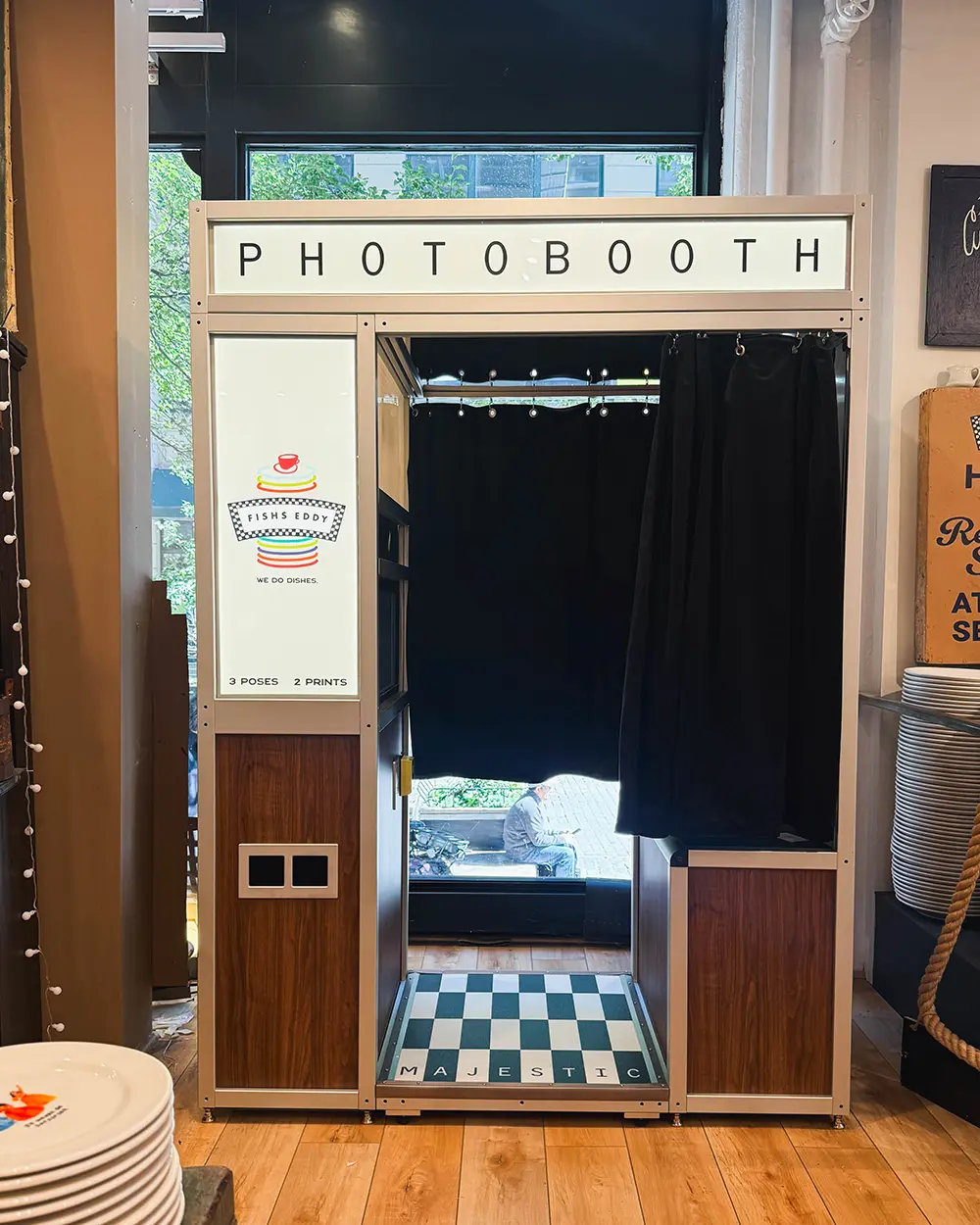 Front of the Fishs Eddy photo booth showing the black velvet curtain, the checkerboard floor plate and the Fishs Eddy logo panel