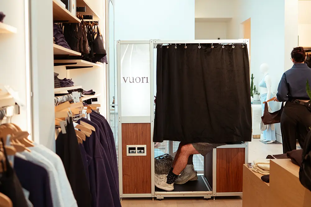 Someone inside the Vuori photo booth with the black curtain drawn, among the clothing racks