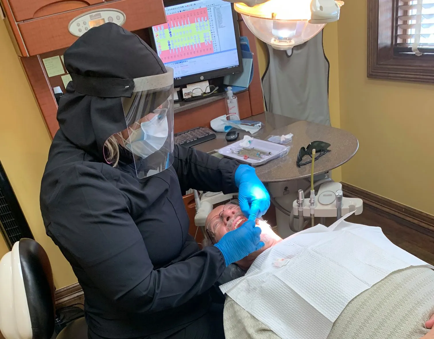 Dental hygienist in PPE cleaning patient's teeth.