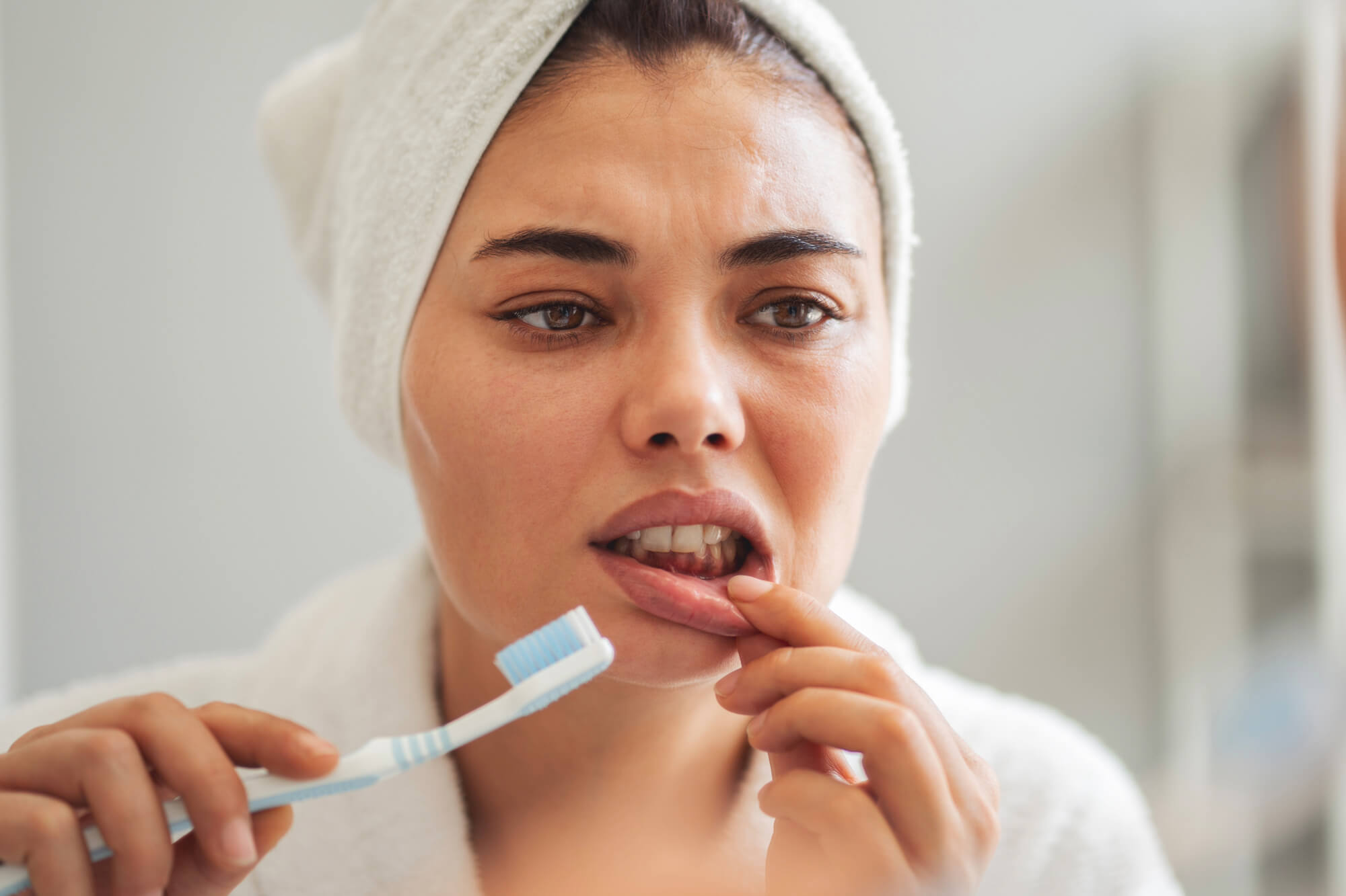Woman examining a sore in her mouth, holding a toothbrush.