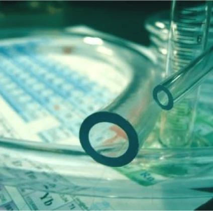 A close-up image of a transparent tube resting on a petri dish with a periodic table and other laboratory equipment visible in the background.