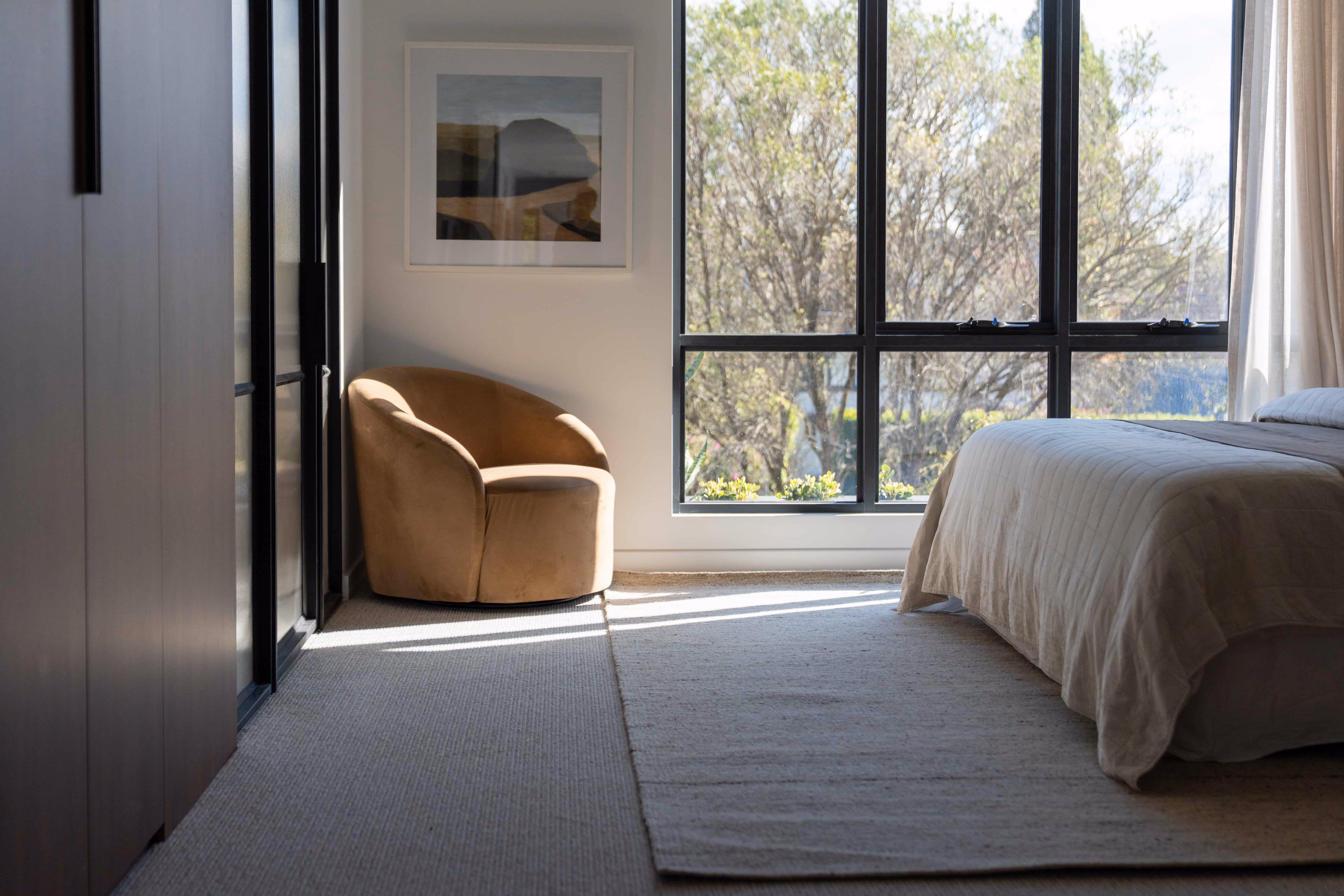 Minimalist bedroom with neutral armchair, bed, and floor-to-ceiling window.