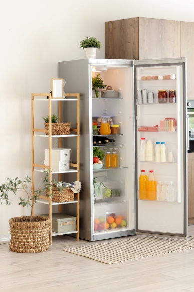 A modern kitchen with a stainless steel refrigerator door open showing organised shelves with fruit, vegetables, bottles, jars, cartons, and eggs inside.