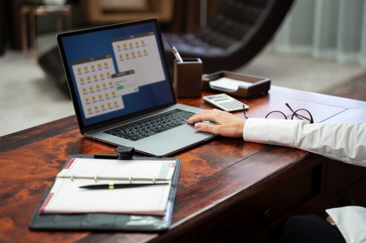 Person working on a laptop with scheduling software and documents on a desk, illustrating Databuzz’s bespoke delivery management system for UK consultancies.
