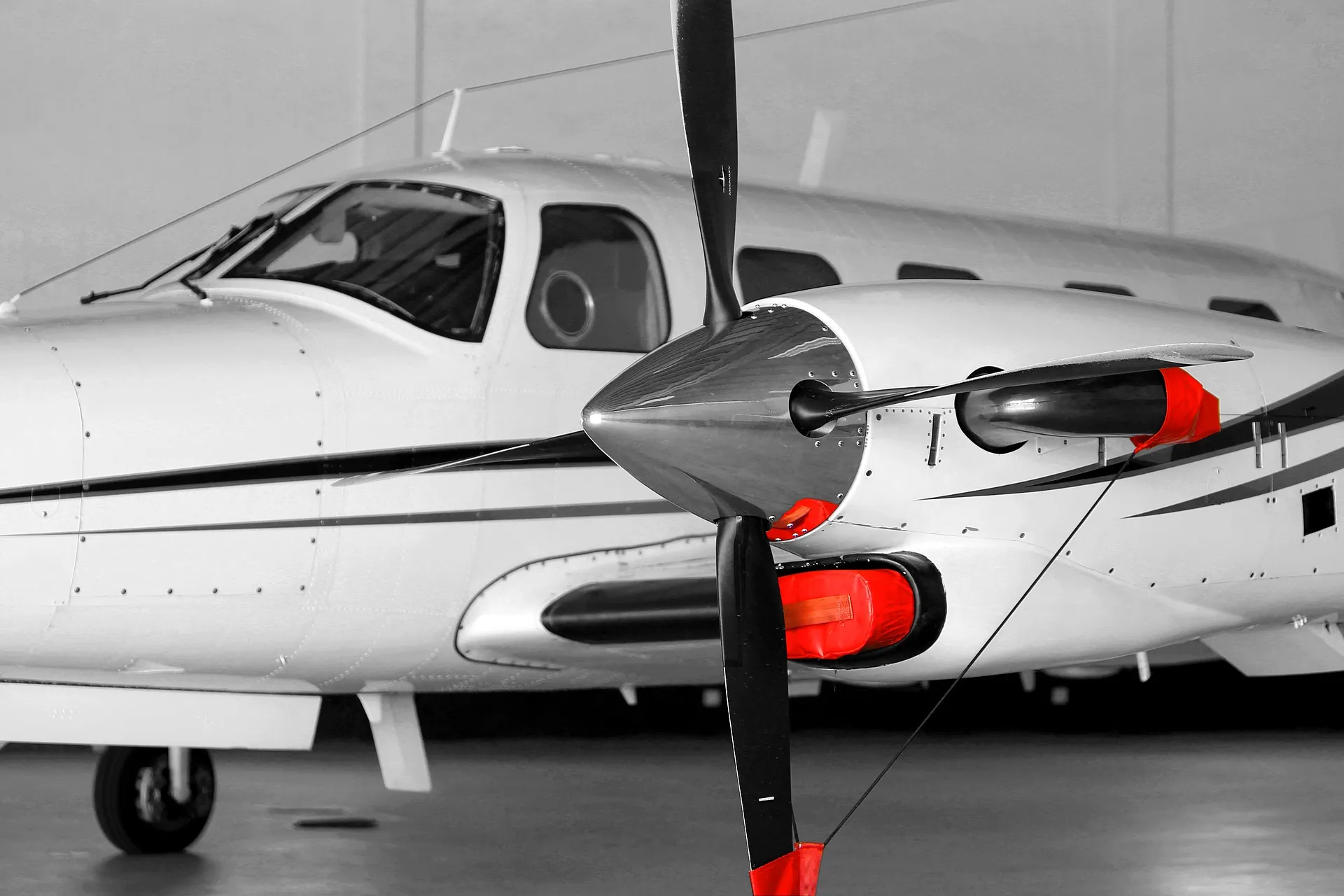 Vue rapprochée d'un avion privé avec une hélice noire à trois pales et des protections rouges sur les parties sensibles du moteur et de l'hélice, posé dans un hangar.