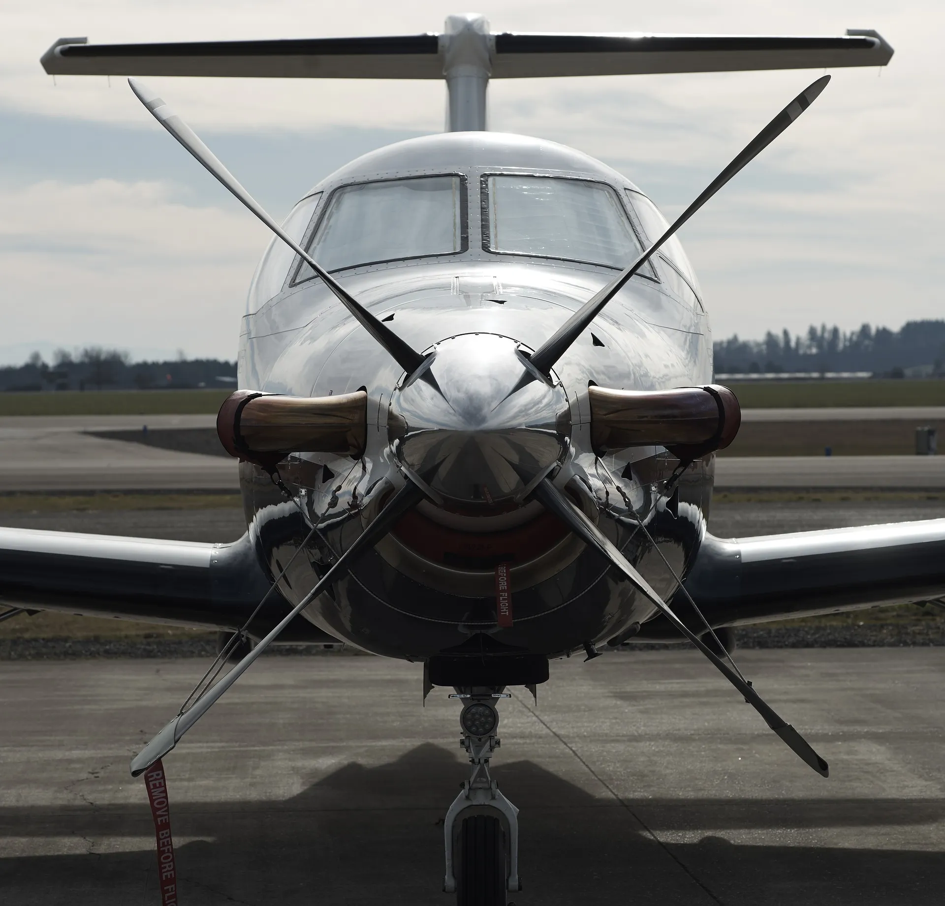 Avion Pilatus PC-12 blanc vu de face sur une piste d'aéroport, avec une hélice à quatre pales en position arrêtée et un ciel nuageux en arrière-plan.