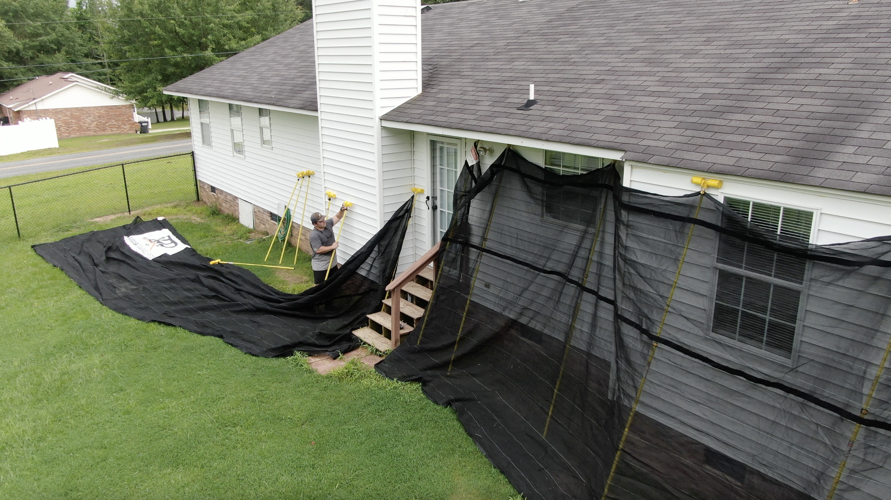 Residential roof replacement in progress with protective tarp installed along side of house