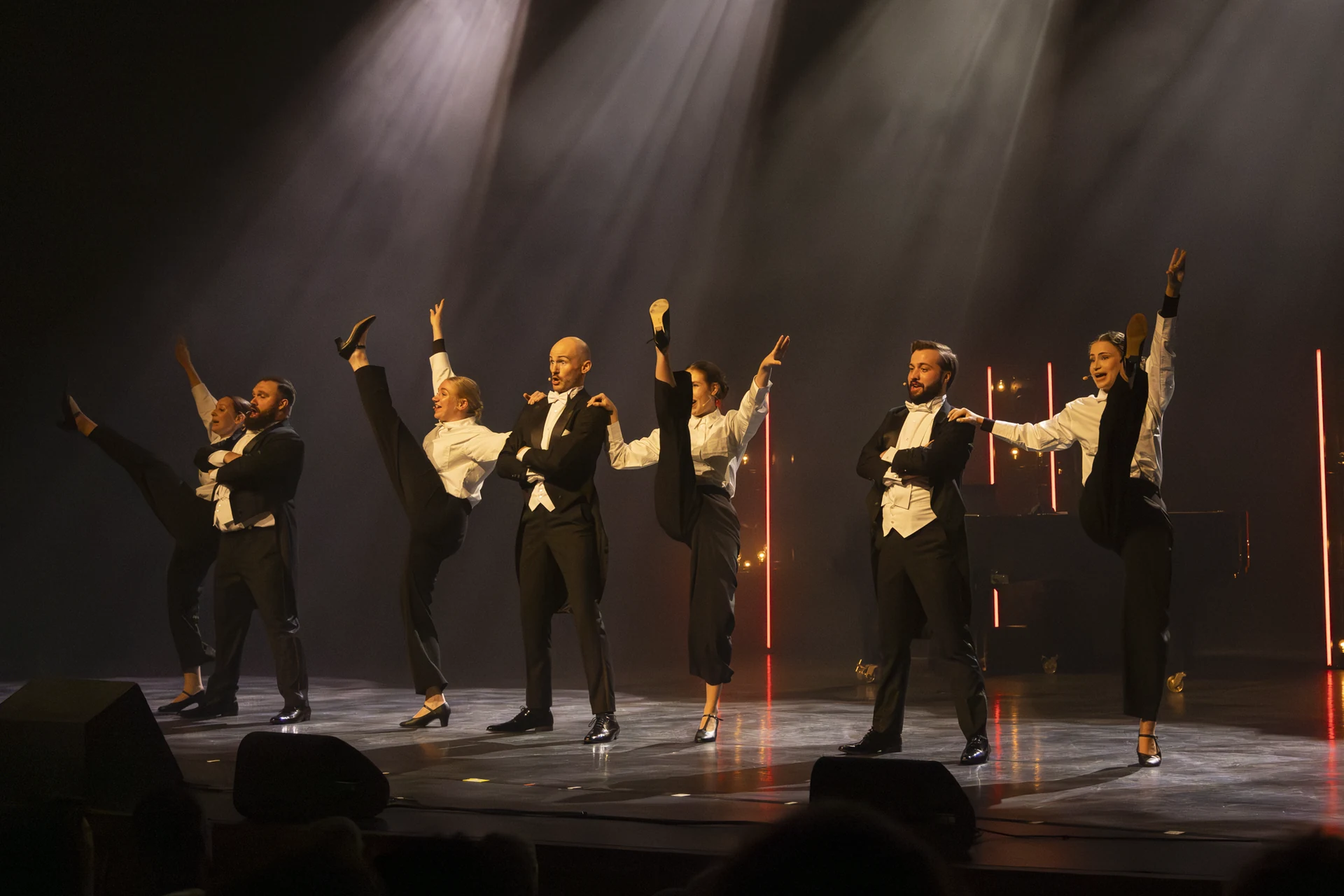 Baritones en dansers voeren samen hoge kicks uit op het podium.