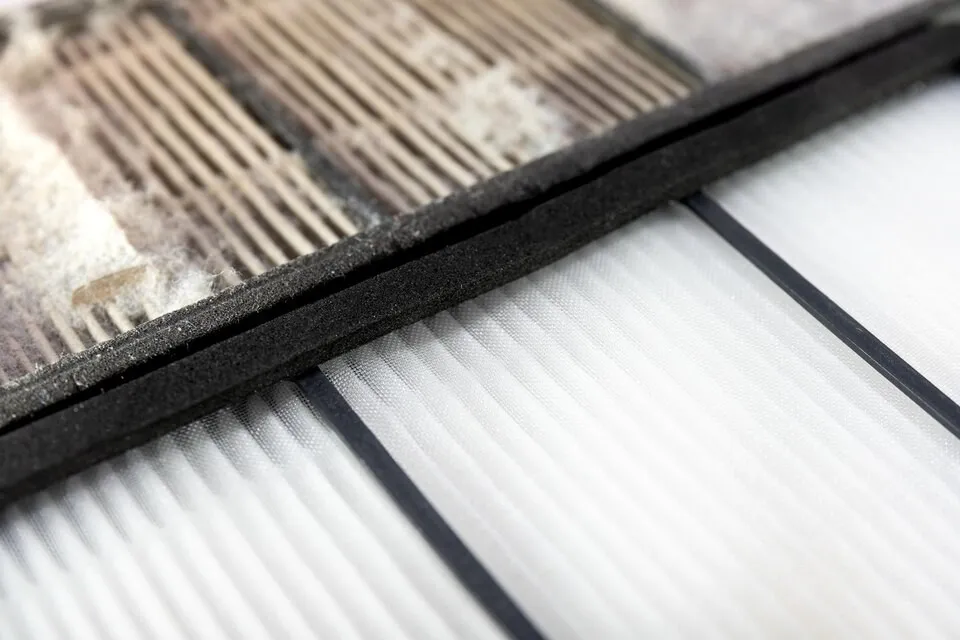 A close-up shot compares a dirty, gray, and dusty HVAC filter with a clean, pleated white filter, showing the clear difference between them.