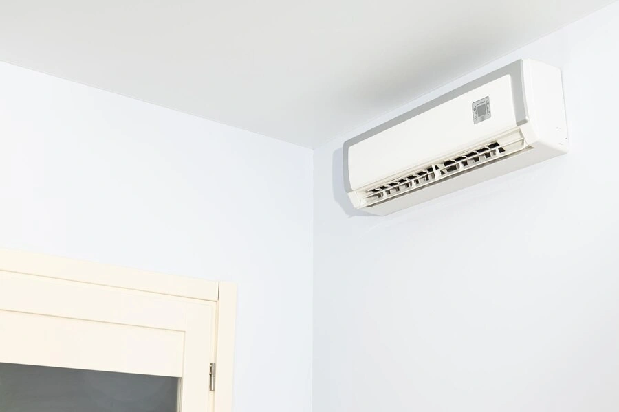 A horizontal white ductless AC unit with a silver trim is mounted high on a white wall above a beige cabinet.
