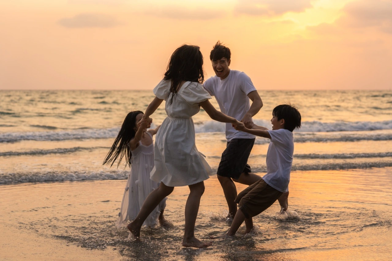 A family of four plays at the beach at sunset.