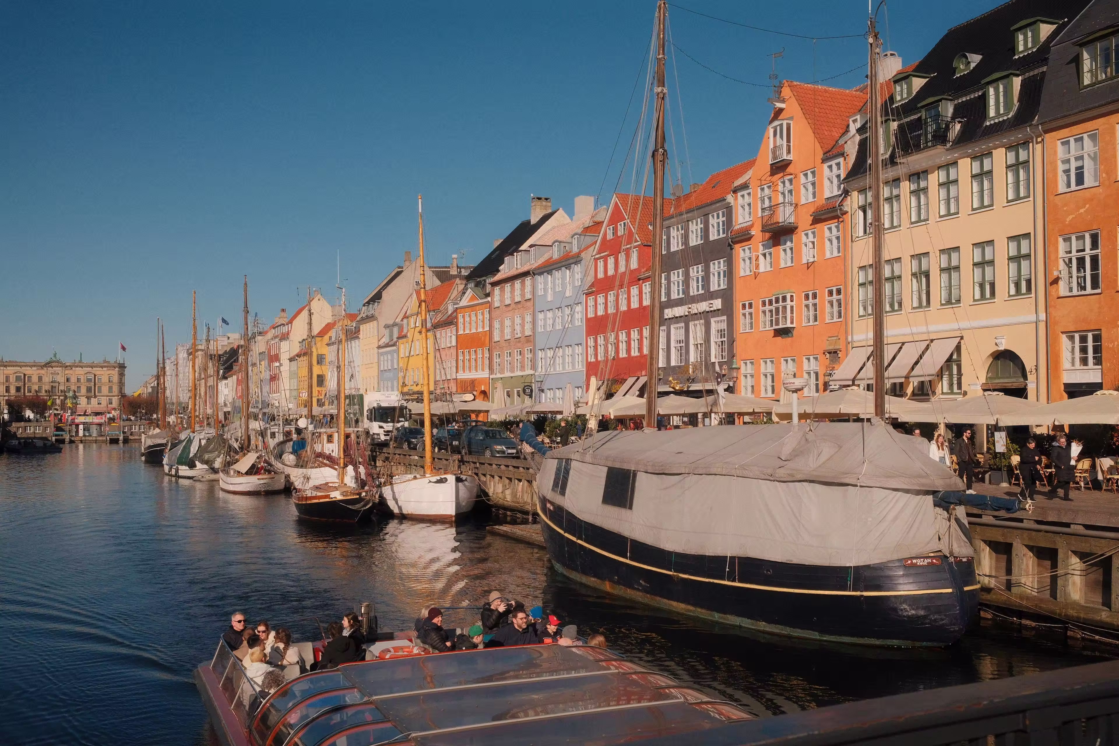 Colorful buildings along a canal with boats docked and a tour boat carrying people under a clear blue sky.