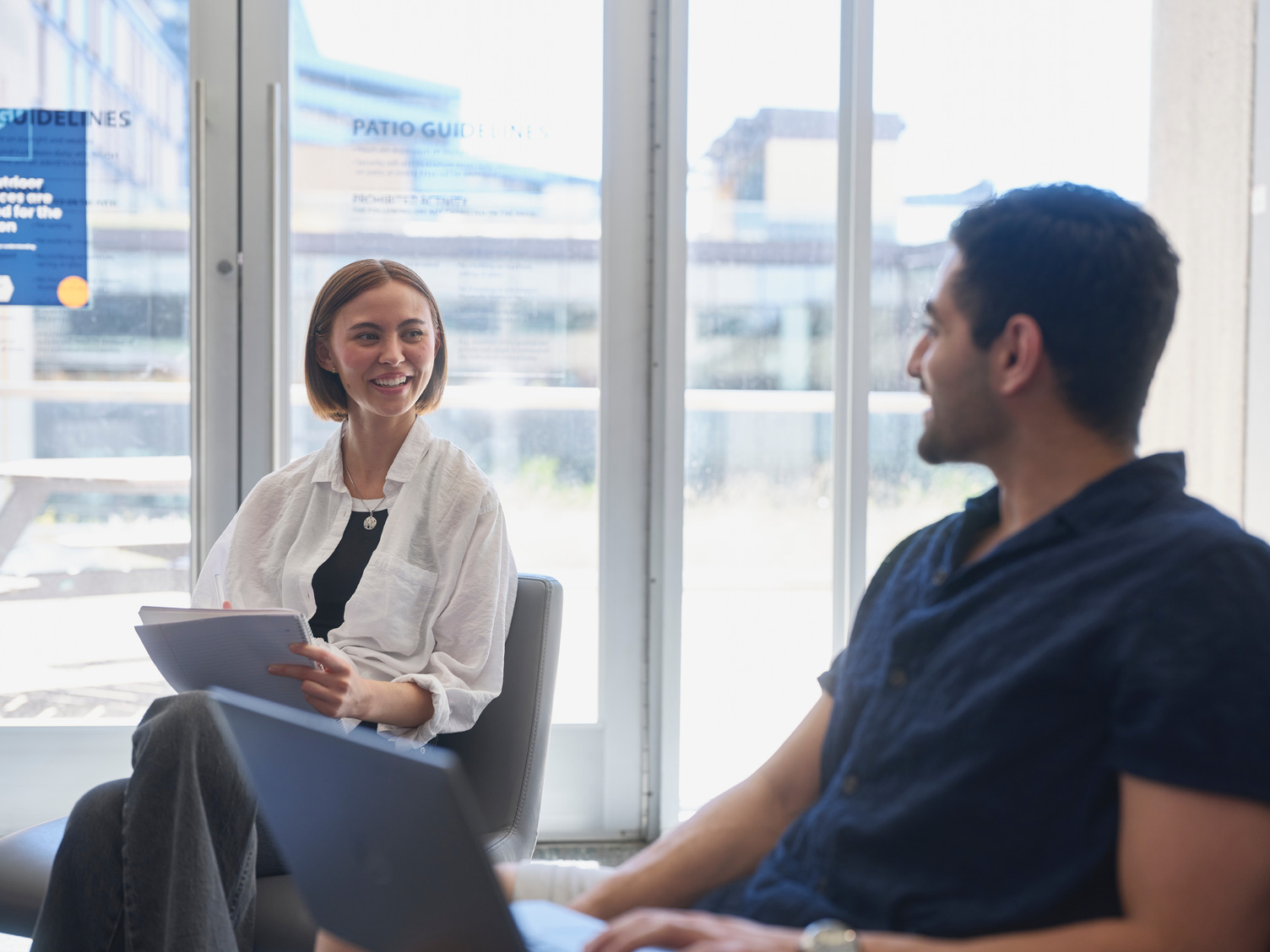 Two students studying together, one of his laptop and the other writing notes in her notebook.