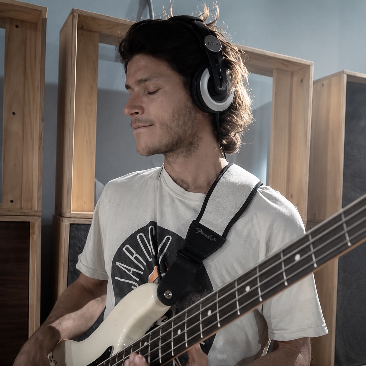 Young man wearing headphones plays electric bass guitar in a room with wooden acoustic panels. One of the teachers.